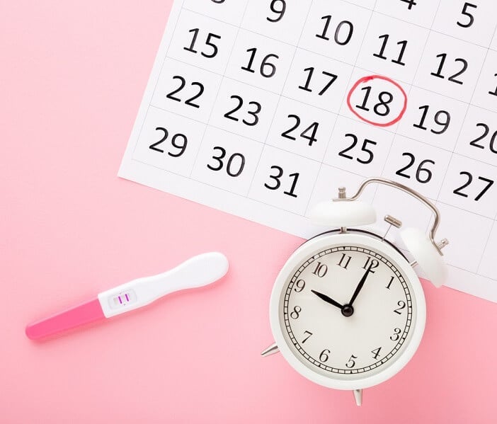 Calendar, clock, pregnancy test on pink background top down